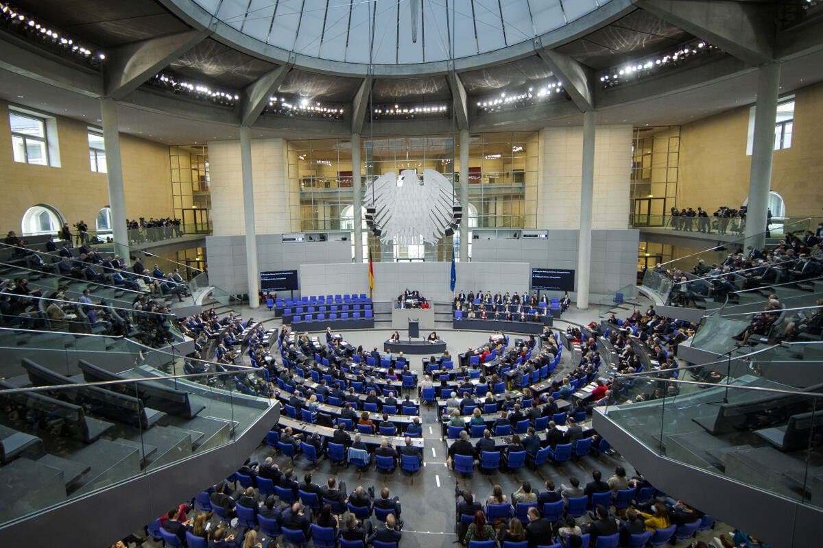 There is a big amphitheater with blue chairs organized in circular rows. There is white flat eagle hanging over the tribune.